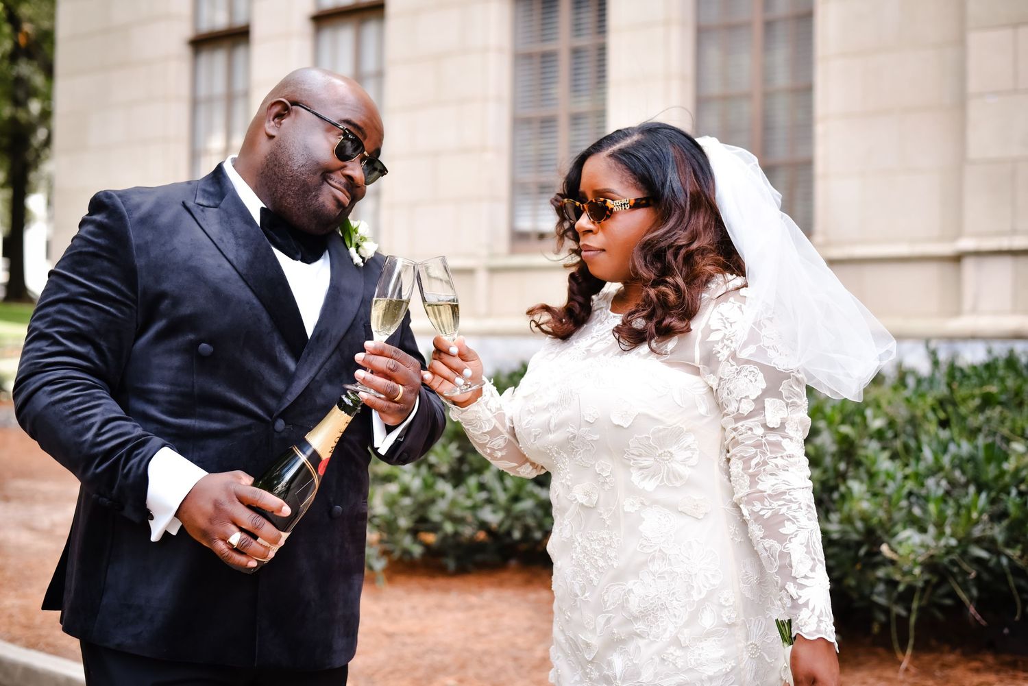Elegant couple in formal wedding attire sharing romantic moments during outdoor photo session at stone building venue.
