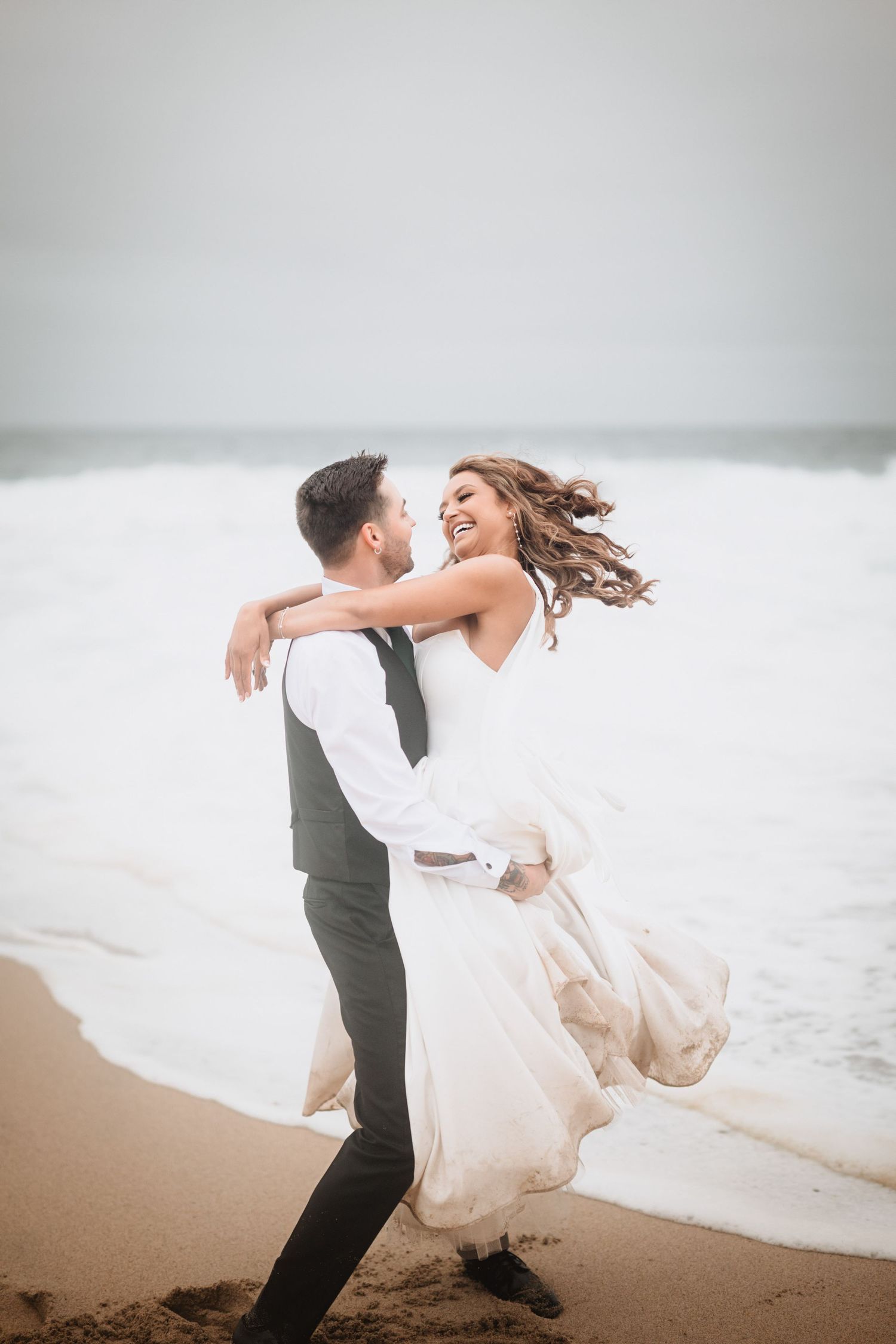 groom lifts up bride and spins her around at the beach during sunset