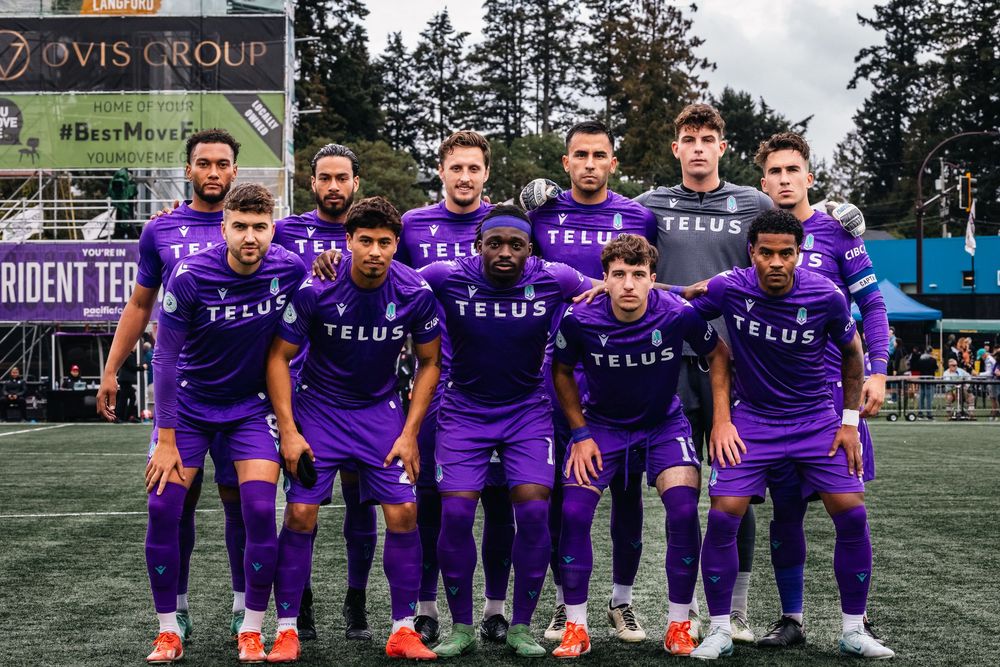 Soccer players in purple jerseys pose together on a grass field during a team photo session.