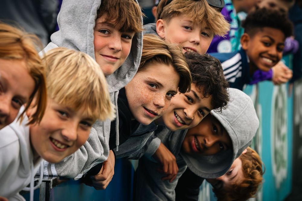Group of young people leaning forward and smiling together in a candid outdoor photo.