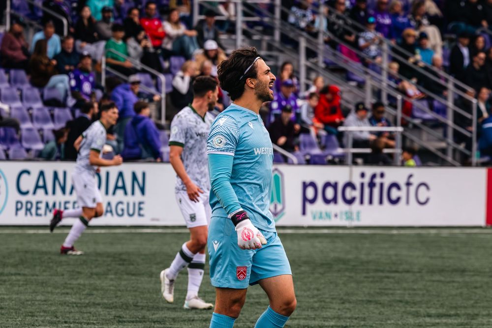 Soccer players in light blue uniforms compete during a match on a professional field with stadium seating visible.