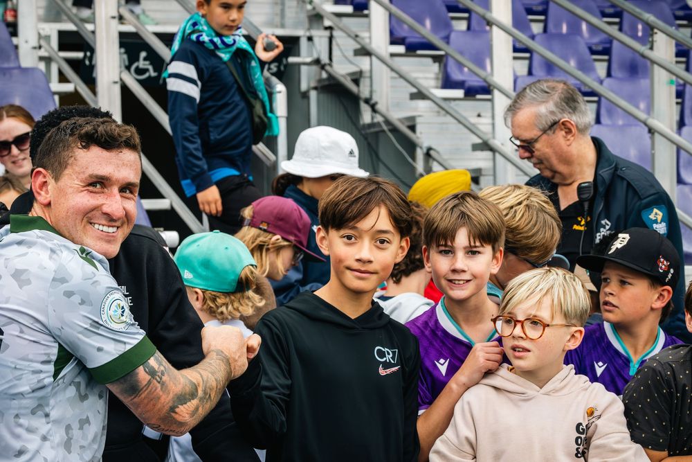 A group of young sports fans smile and gather together in stadium bleachers during a sporting event.