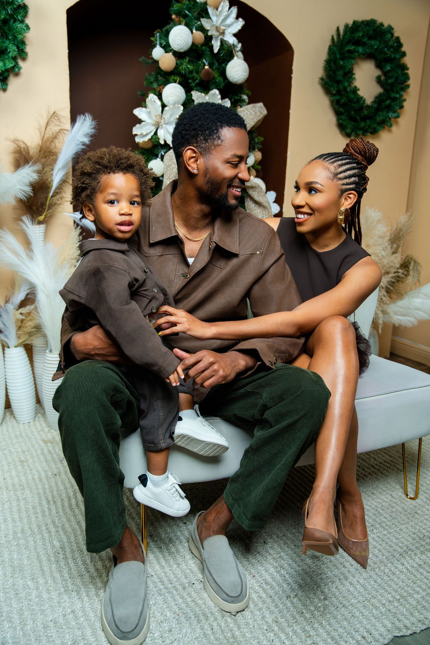 A family wearing coordinated brown outfits poses playfully on a carpeted floor with holiday decorations in the background.