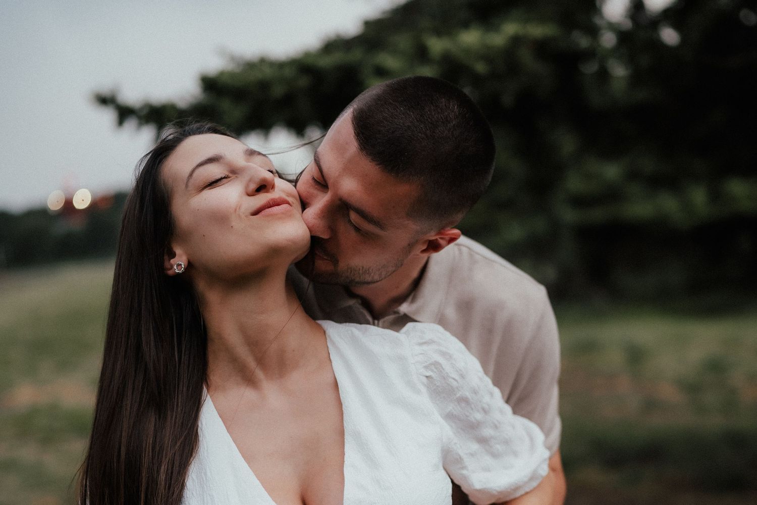 A couple shares an intimate moment outdoors in a natural setting at dusk.