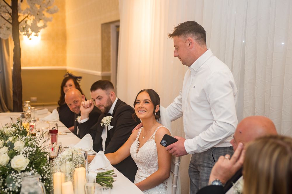 Candid moment of laughter during wedding reception speeches at an elegantly decorated banquet table.