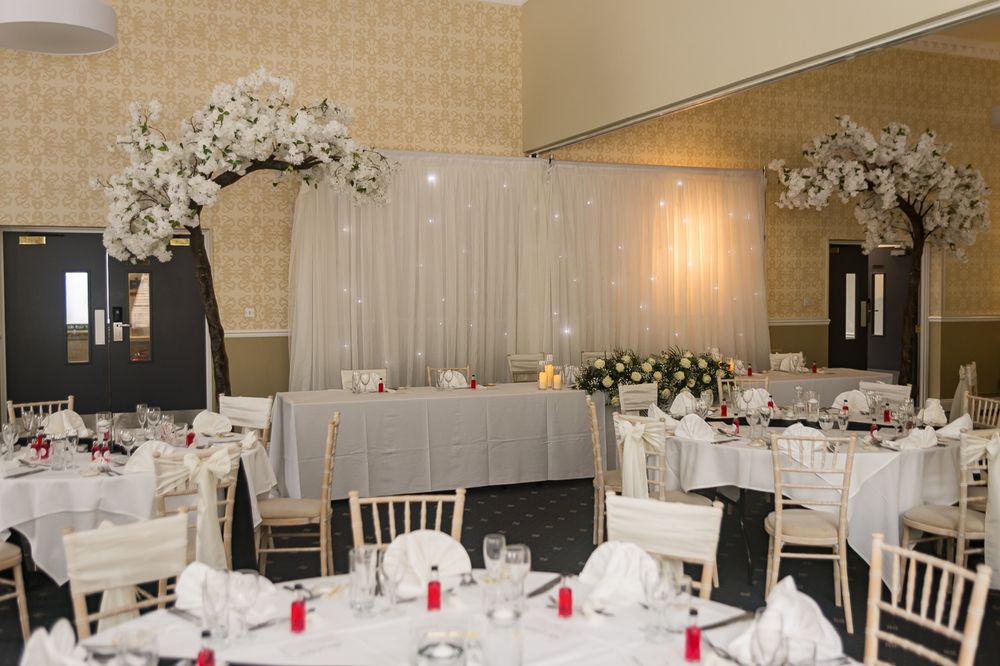 An elegant wedding reception room with white-clothed tables and floral centerpieces.