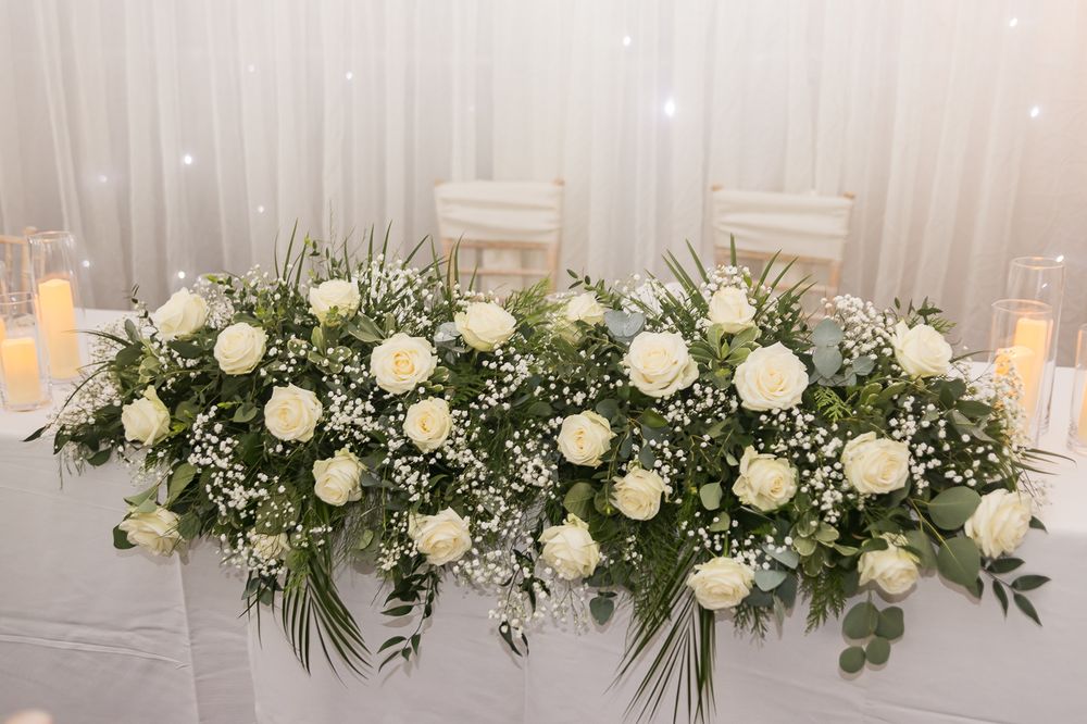 Elegant white floral centerpiece arrangement with roses and greenery adorning a wedding reception table.