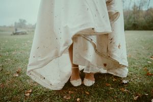A series of four photos showing the hem of a white dress and feet walking through grass and autumn leaves.