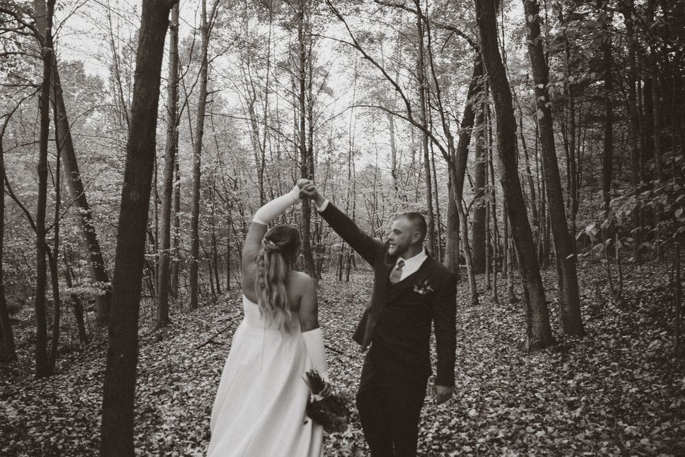 A couple in wedding attire dancing together in a misty forest setting, captured in black and white.