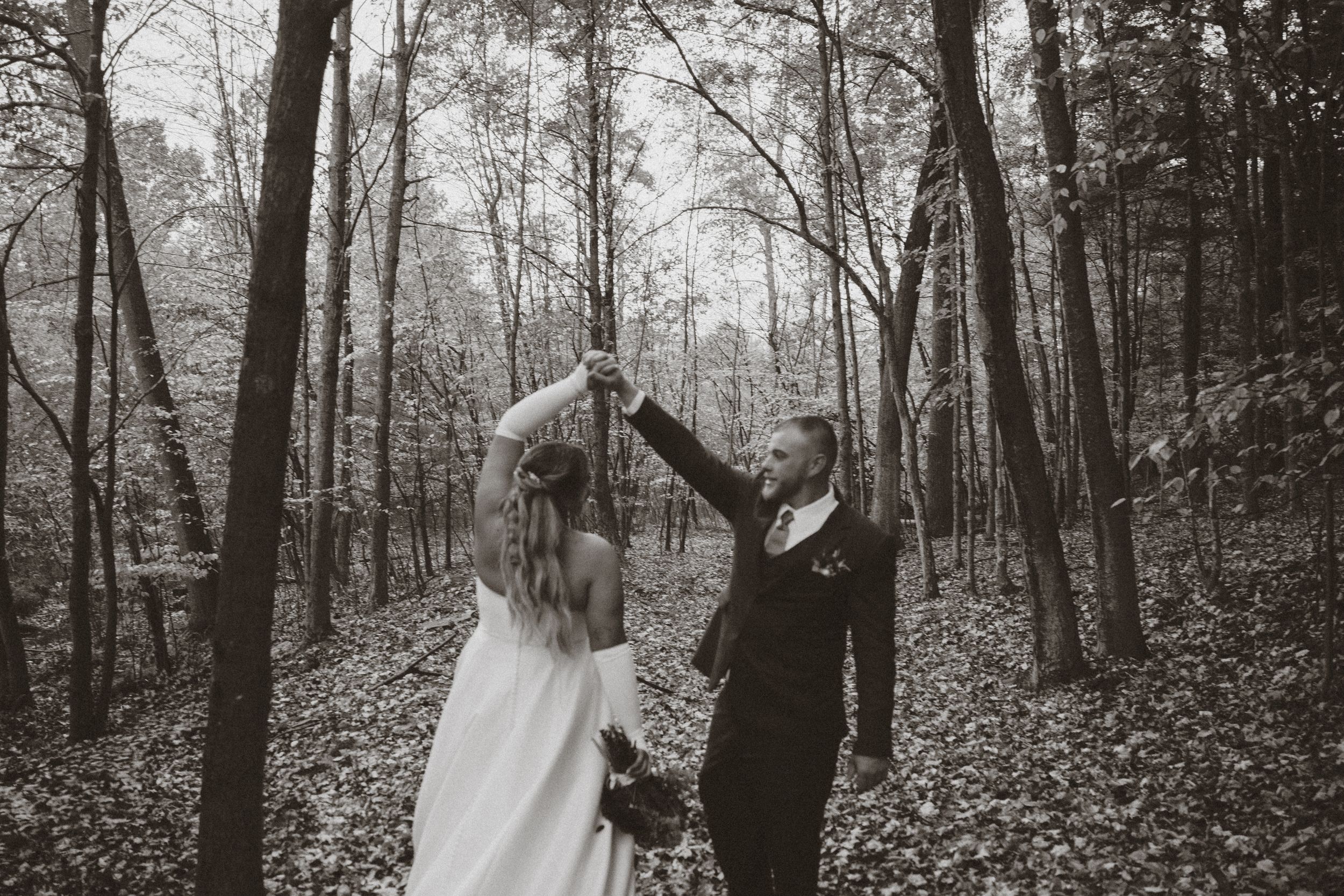A couple in wedding attire dancing together in a misty forest setting, captured in black and white.