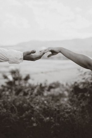 A black and white artistic photograph shows two hands reaching towards each other against a blurred background.