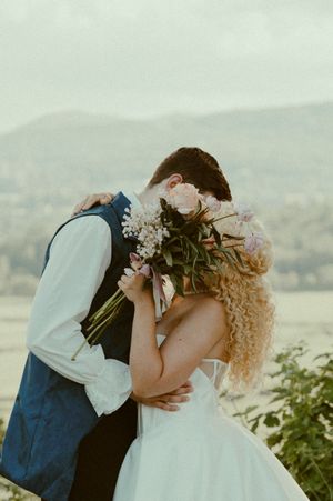 A romantic wedding couple embracing outdoors with mountains in the background during golden hour.