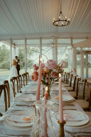 Elegant wedding reception tables set with white linens, pink candles, and floral centerpieces under a draped tent ceiling.