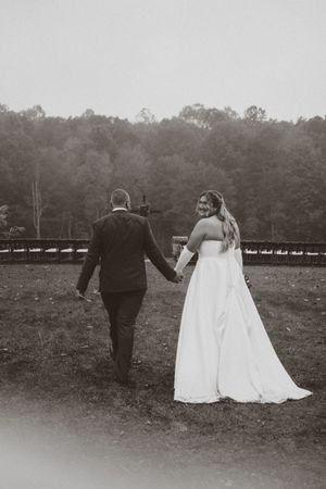 A couple in wedding attire walks together across a scenic field in a series of black and white photos.