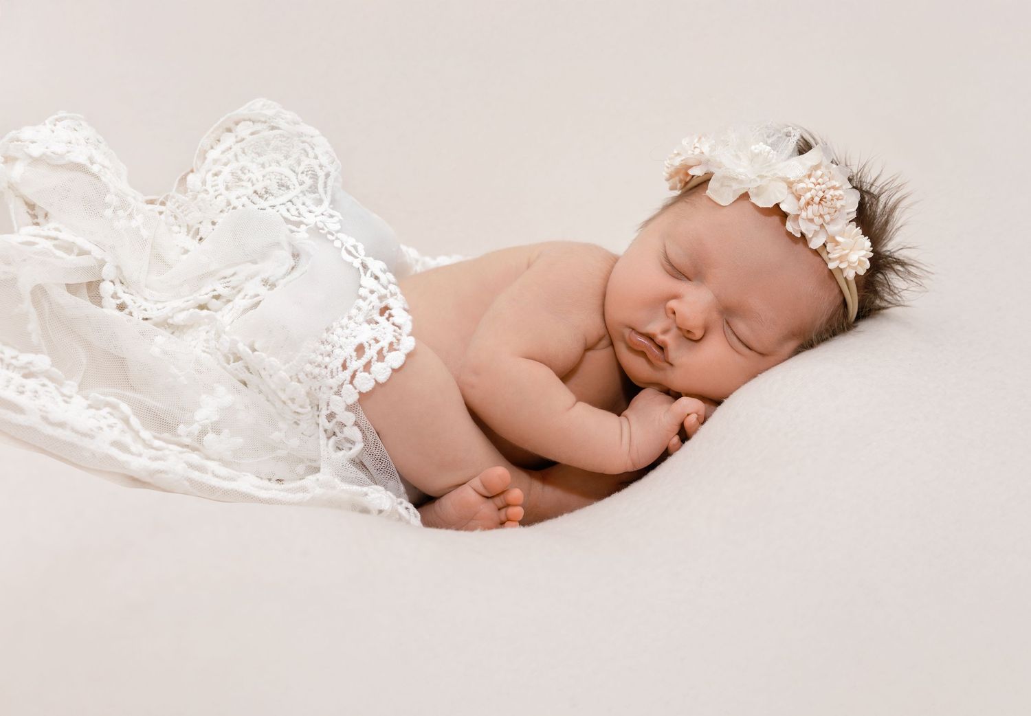A peaceful sleeping newborn baby wrapped in soft pink fabric lies on a light beige background.
