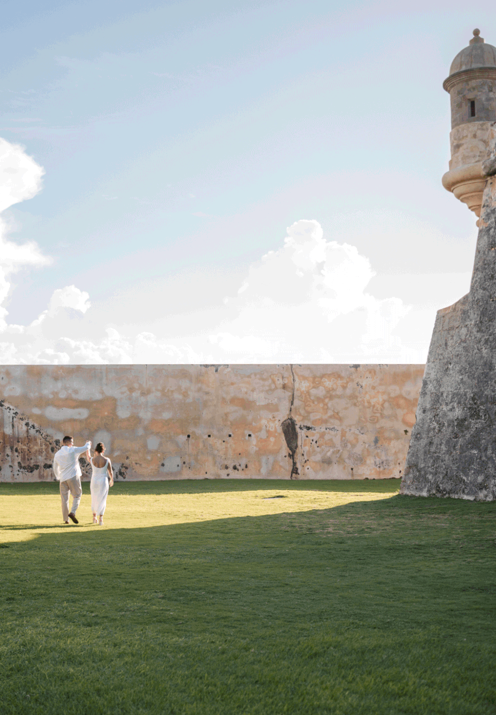Couple walking across open grass near historic fort in Old San Juan Puerto Rico