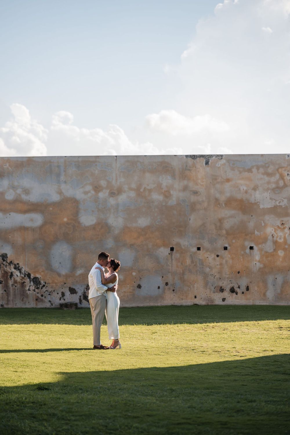 Couple standing in open field near historic fortress wall in Old San Juan Puerto Rico