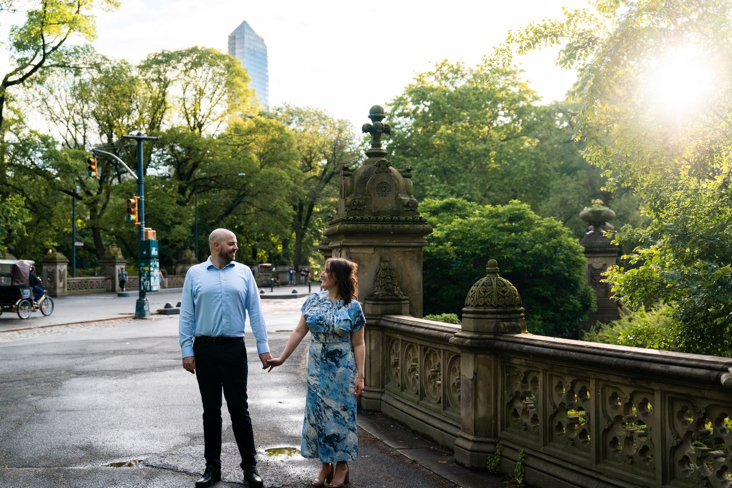 Couple walking hand in hand through sun-dappled Central Park pathway at golden hour.
