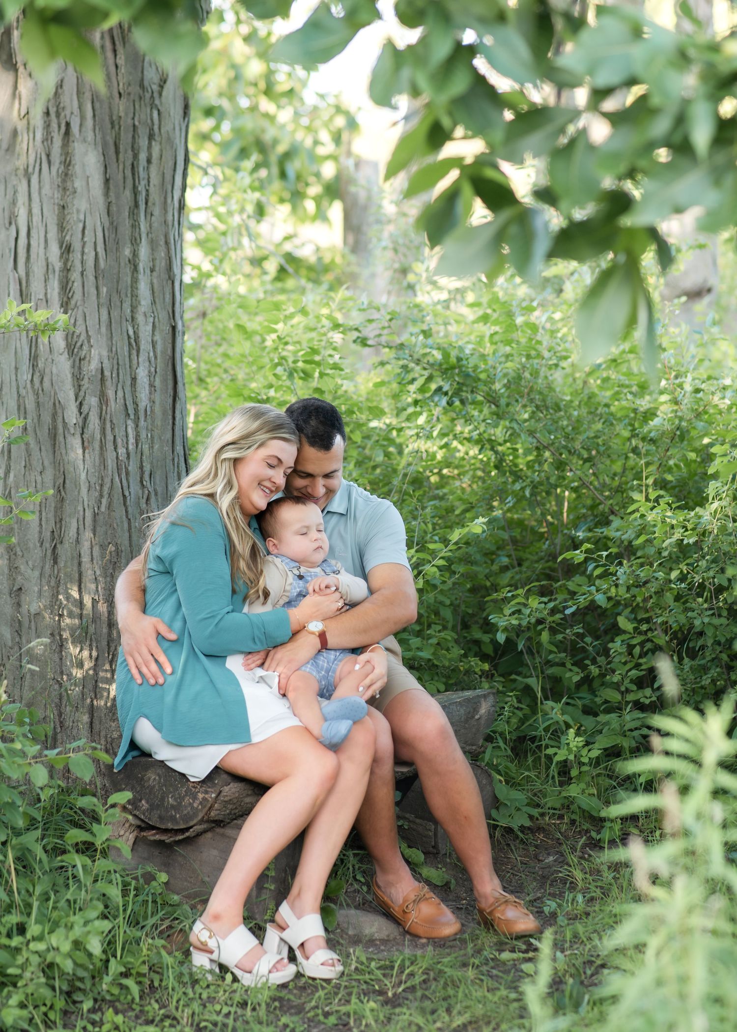 A couple poses in a beautiful pine forest setting during a maternity photoshoot in natural lighting.