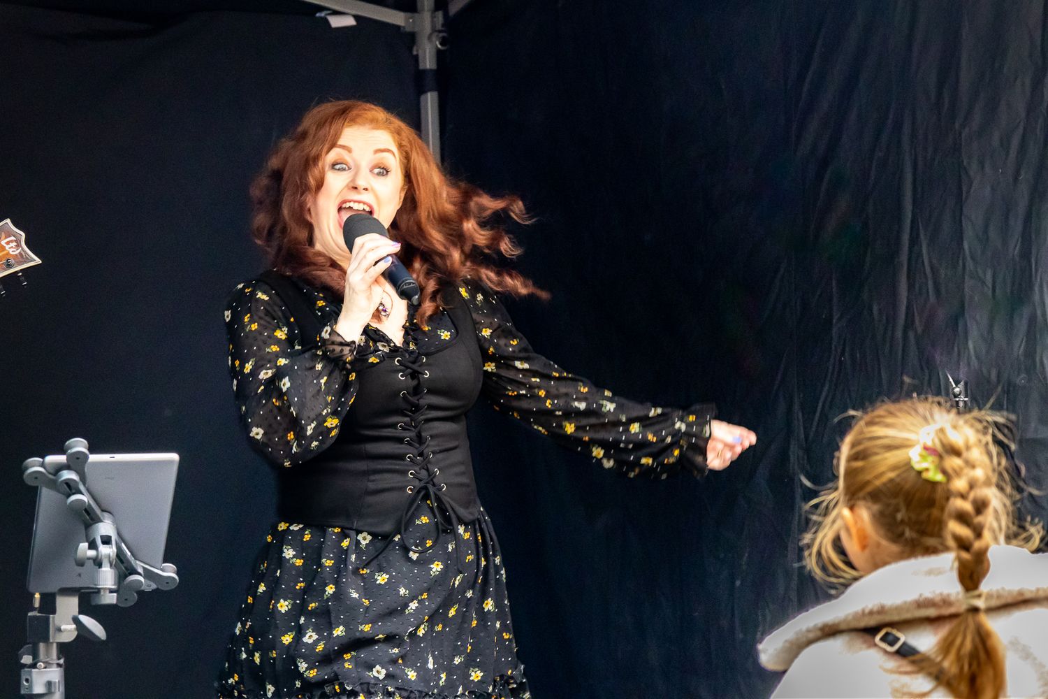 Female singer with curly red hair, singing on stage with a microphone. Her movement is captured in her hair and her expressive face mid-song