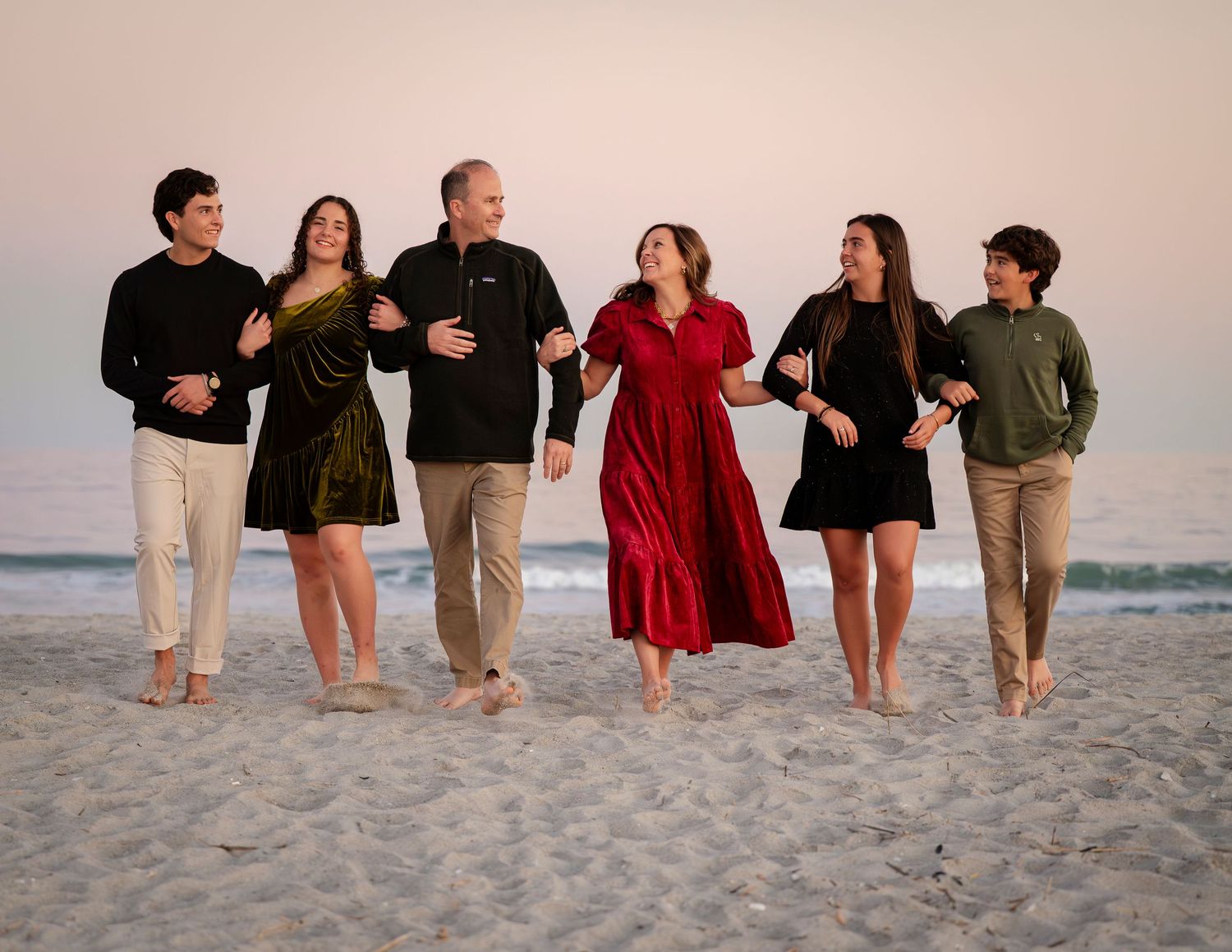 Family group relaxing together on sandy beach at sunset in casual attire.