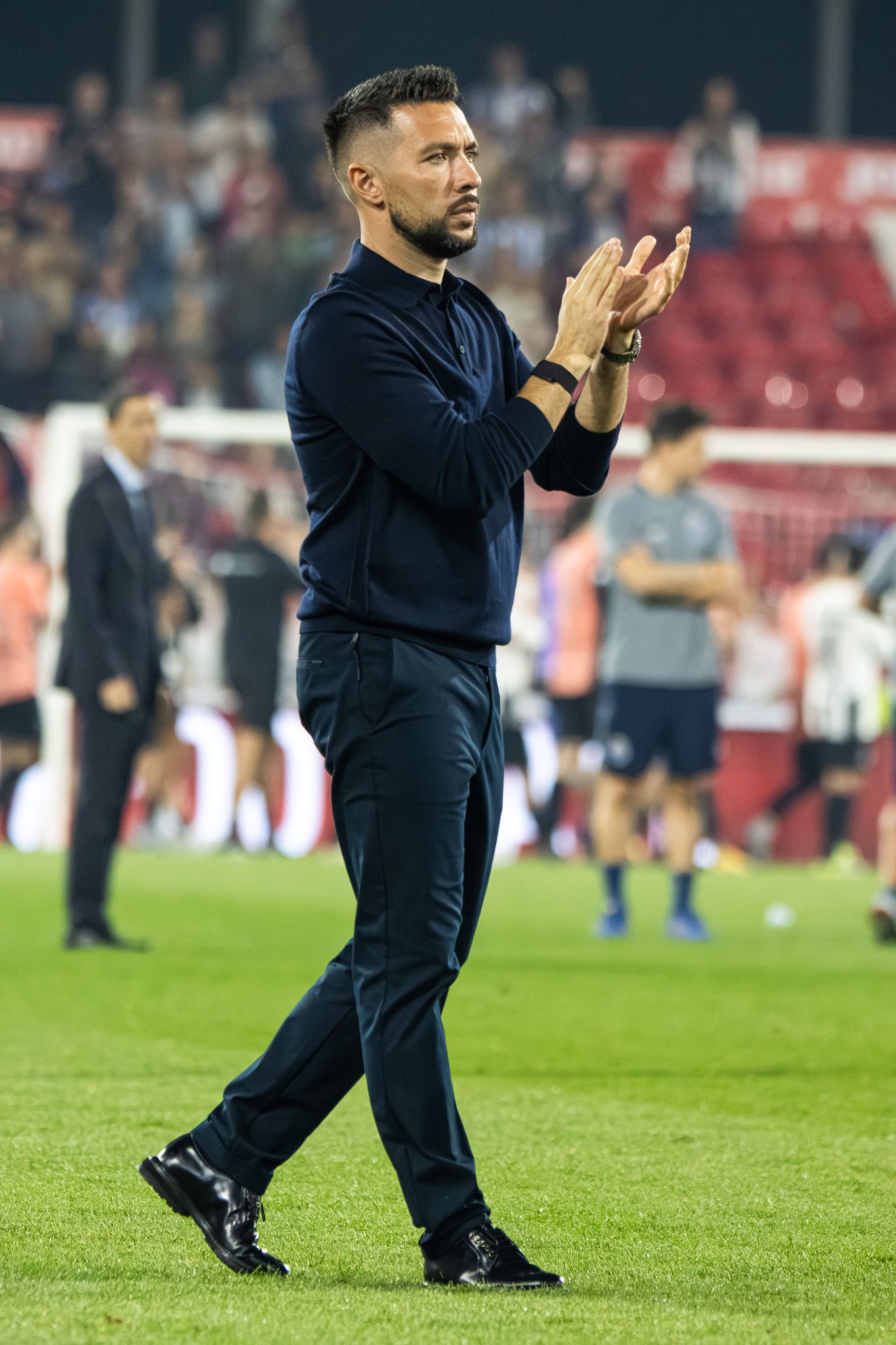 Coach in dark clothing gestures from the sidelines during a soccer match.