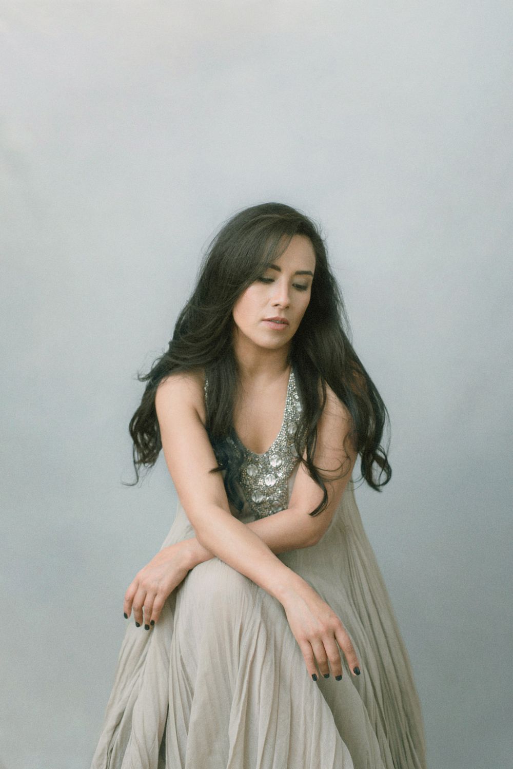 A person in a silver sequined top and flowing beige dress poses gracefully against a light background.