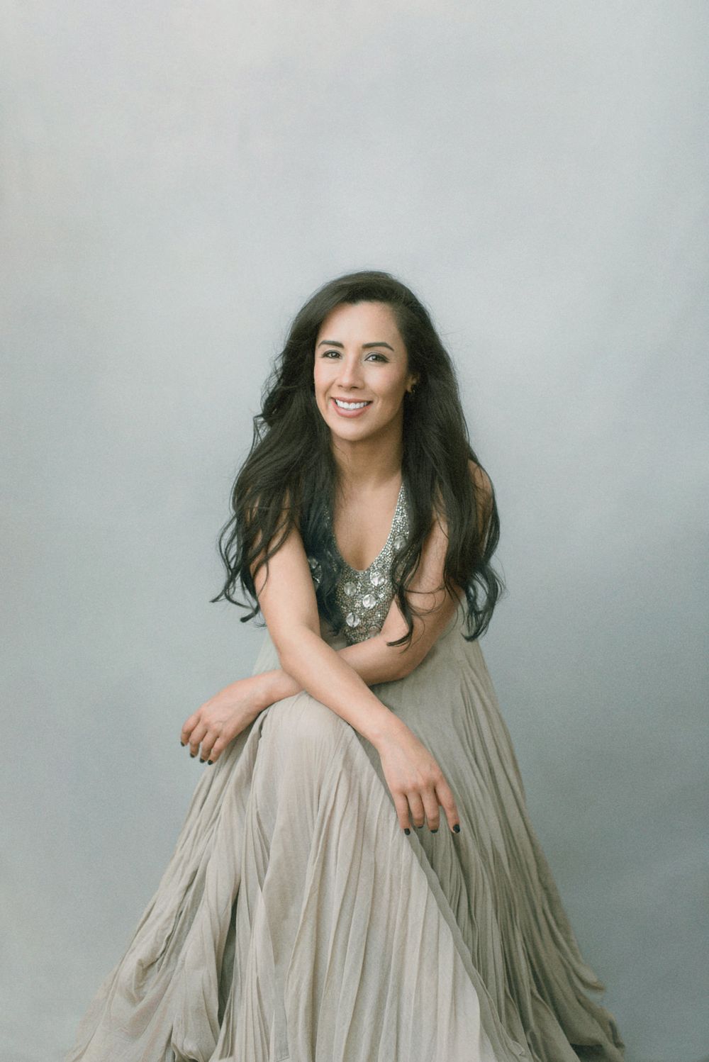 A person in a flowy grey dress poses playfully against a light grey backdrop in a photo series.