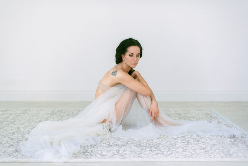 A person in white loungewear poses gracefully on a light gray background in a minimalist photo series.