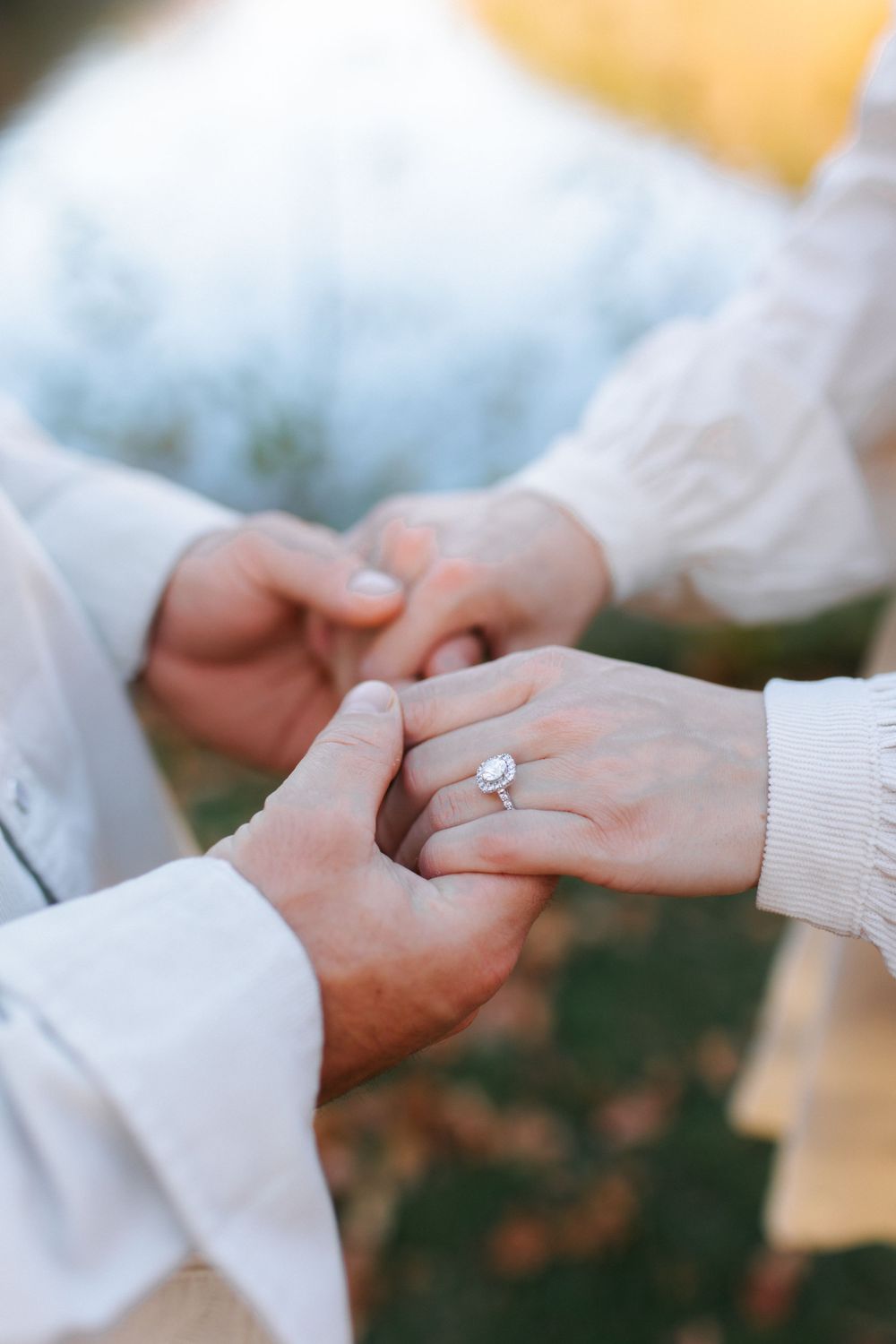 Close-up of hands holding a sparkling engagement ring against a soft, blurred background.