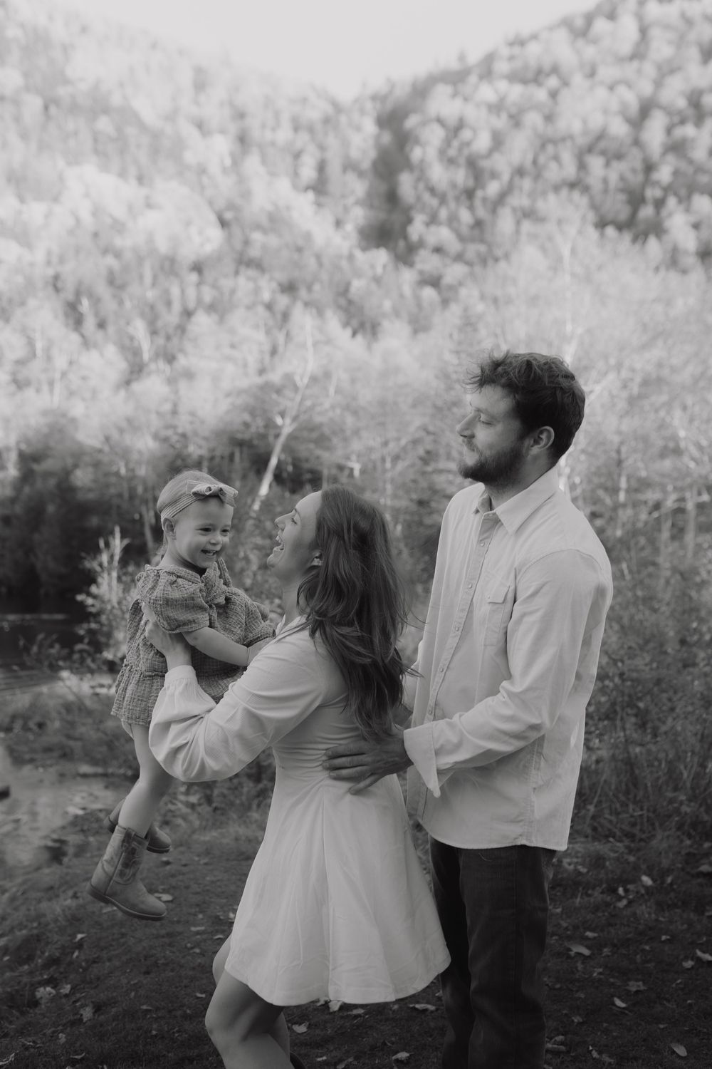 A romantic couple in white clothing dance together in a dreamy black and white outdoor setting with trees in the background.