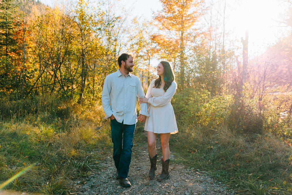 Two people walk together on a sunlit autumn path surrounded by golden foliage and warm evening light.