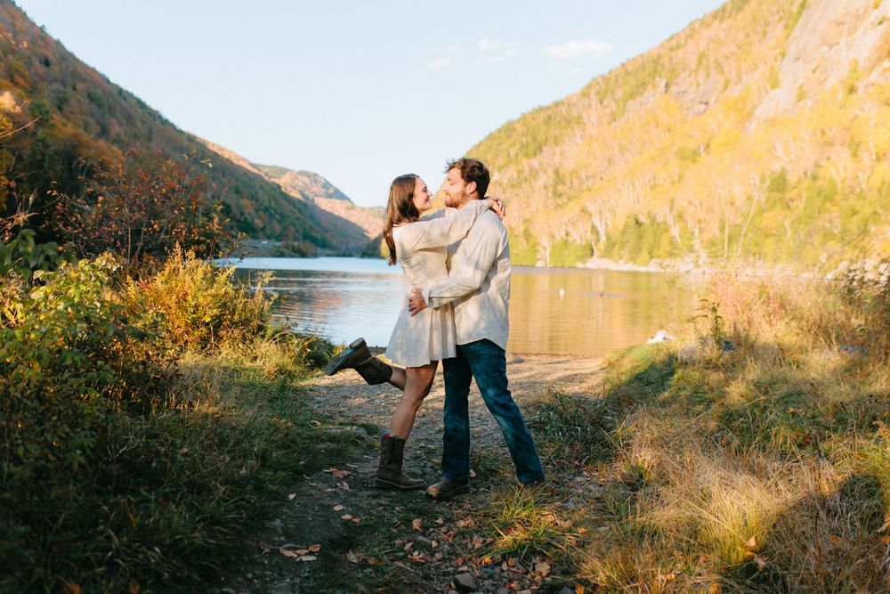 Couple sharing a romantic moment along a scenic mountain lake trail during golden hour.