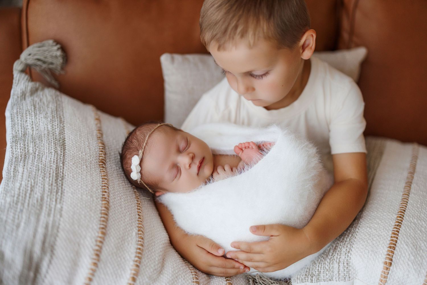 Tender moment between parent and newborn baby swaddled in white blanket against soft neutral backdrop.