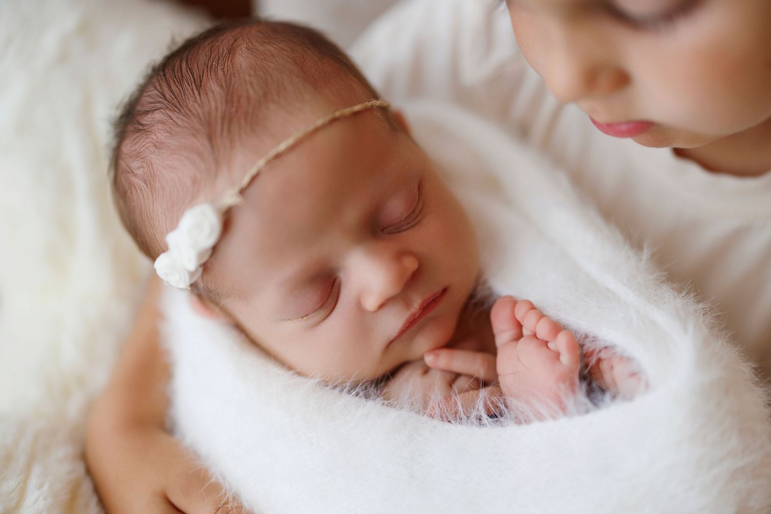 Peaceful sleeping newborn baby in soft white bedding with delicate features and closed eyes.