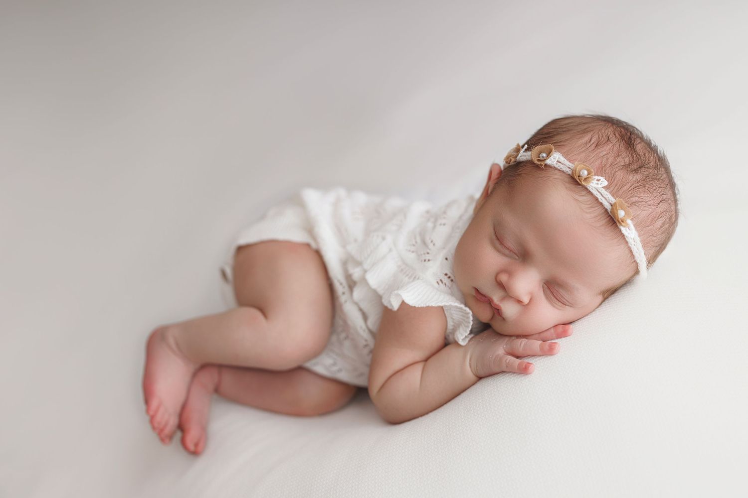 A sleeping newborn baby in white swaddle cloth and headband lying on soft fabric in a creative photo collage.