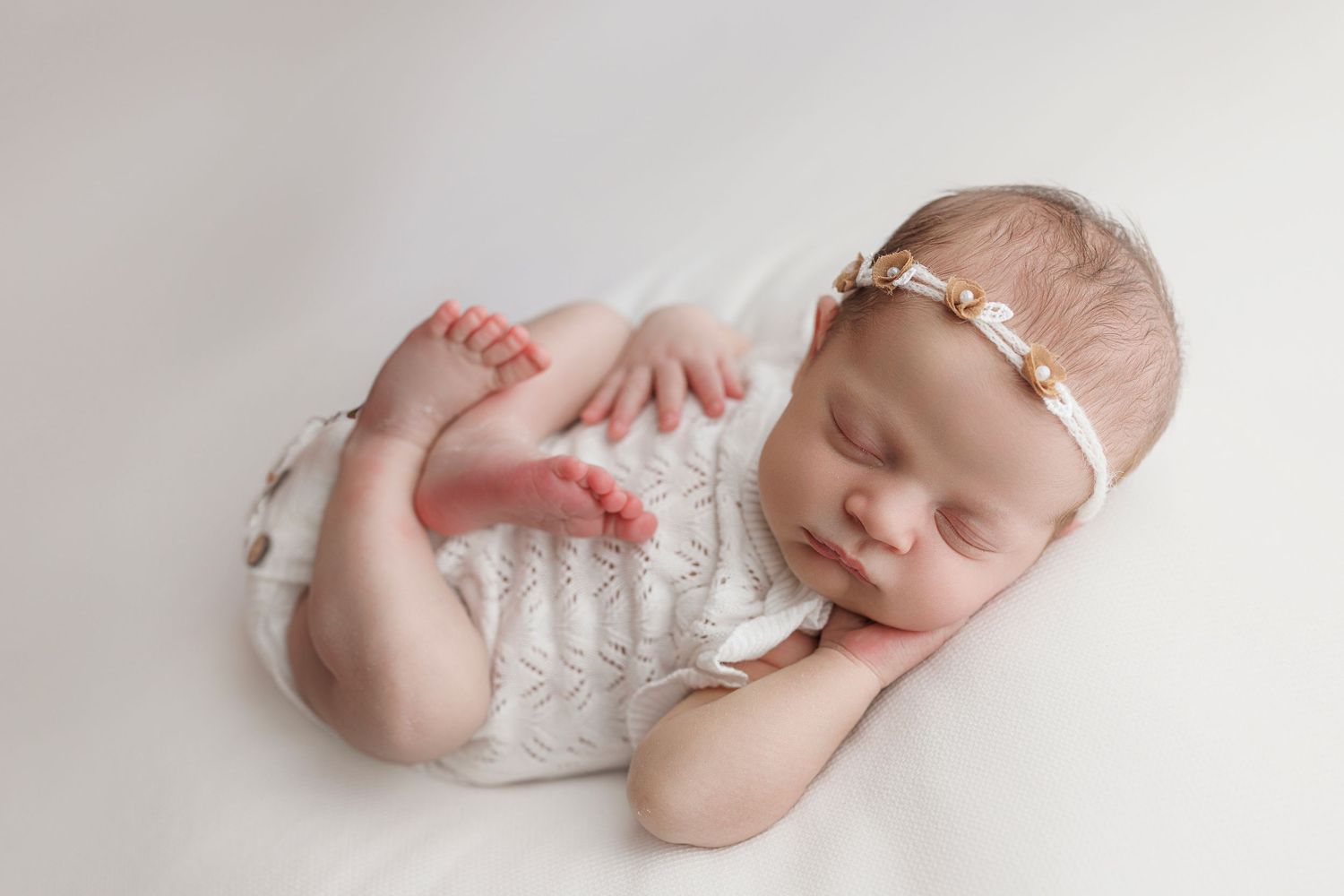 A sleeping newborn in a white lace wrap poses peacefully on a light backdrop during a professional photography session.