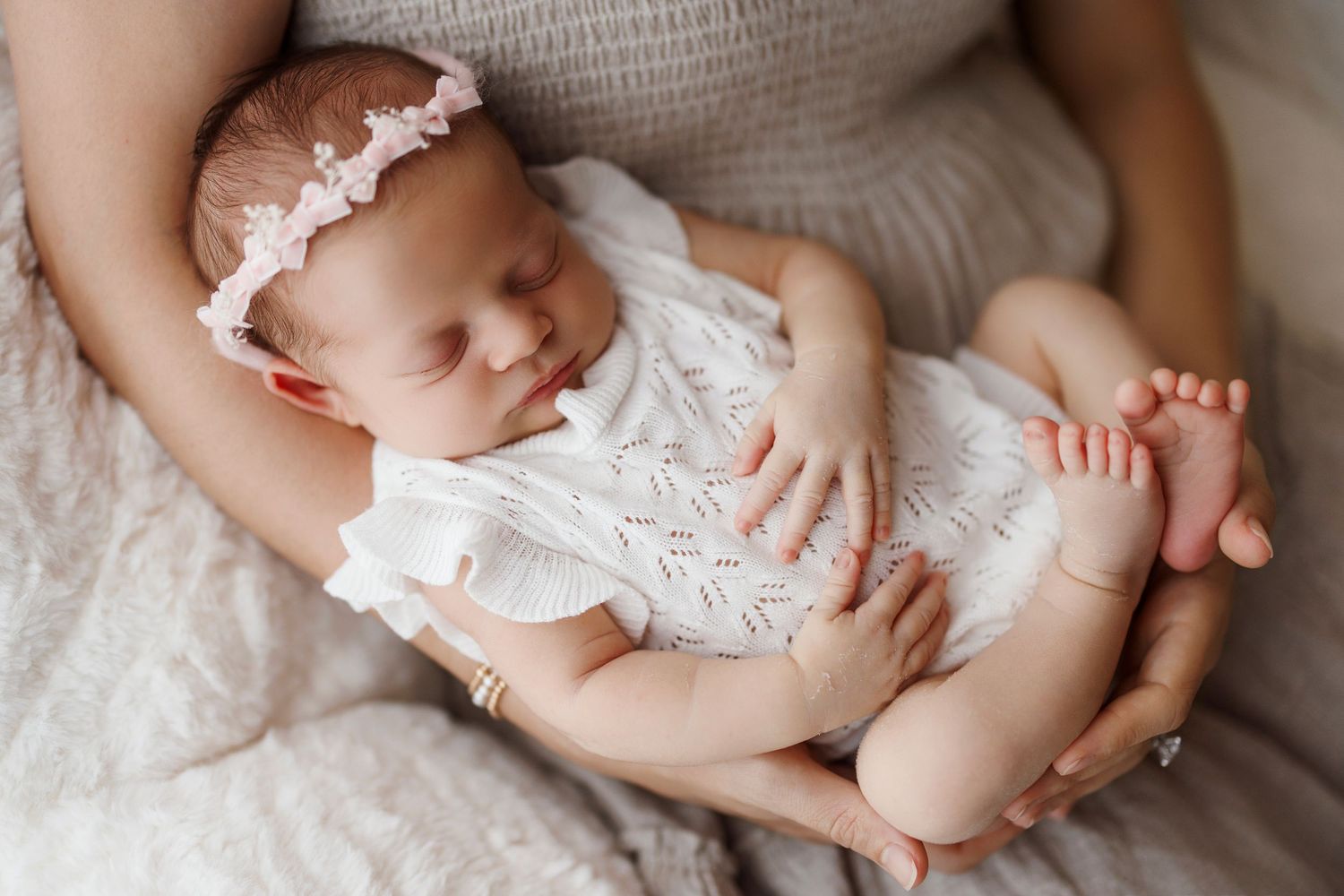 A series of newborn baby photos showing tiny feet, hands, and delicate white lace clothing details against a soft white backdrop.
