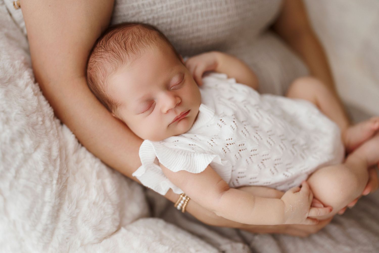 Newborn baby sleeping peacefully in white swaddle blanket while being cradled in gentle arms.