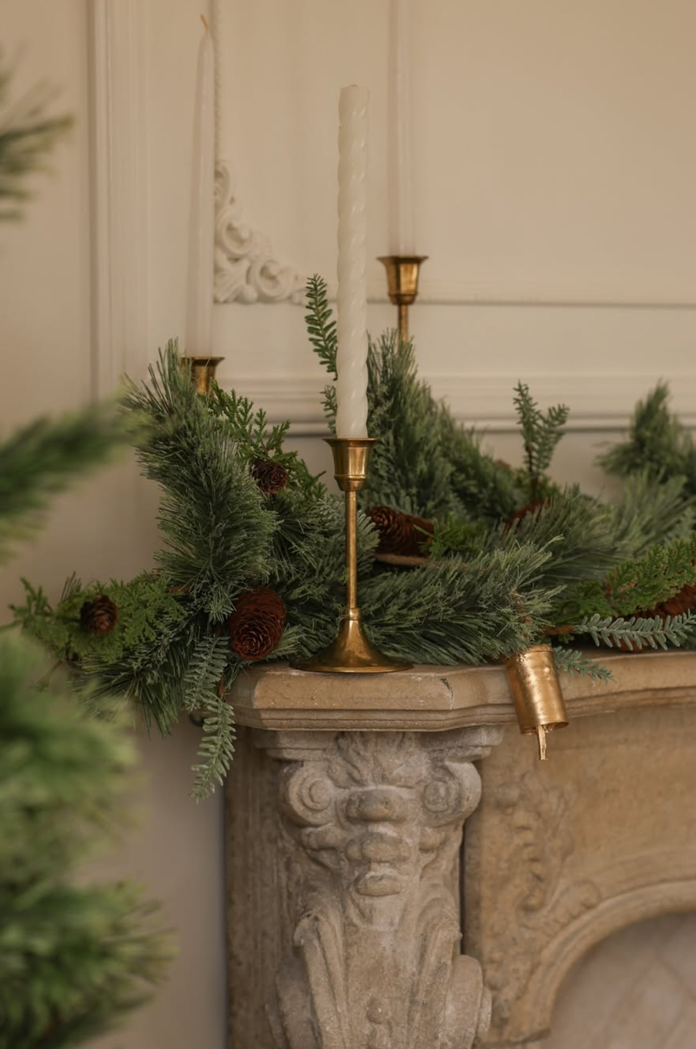 Elegant stone mantle decorated with evergreen branches, pinecones, and brass candlesticks for Christmas.