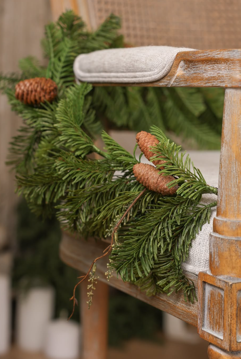 Pine branches with brown pinecones decorate a rustic white-washed wooden chair in a festive holiday display.