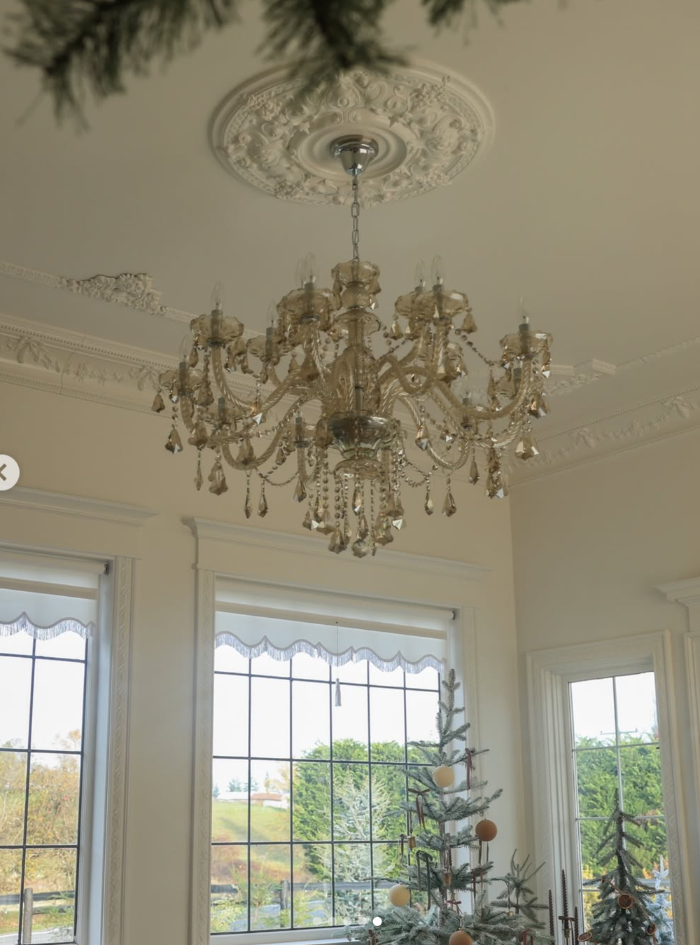 Elegant white dining room with crystal chandeliers, ornate crown molding, and large windows overlooking a scenic landscape.