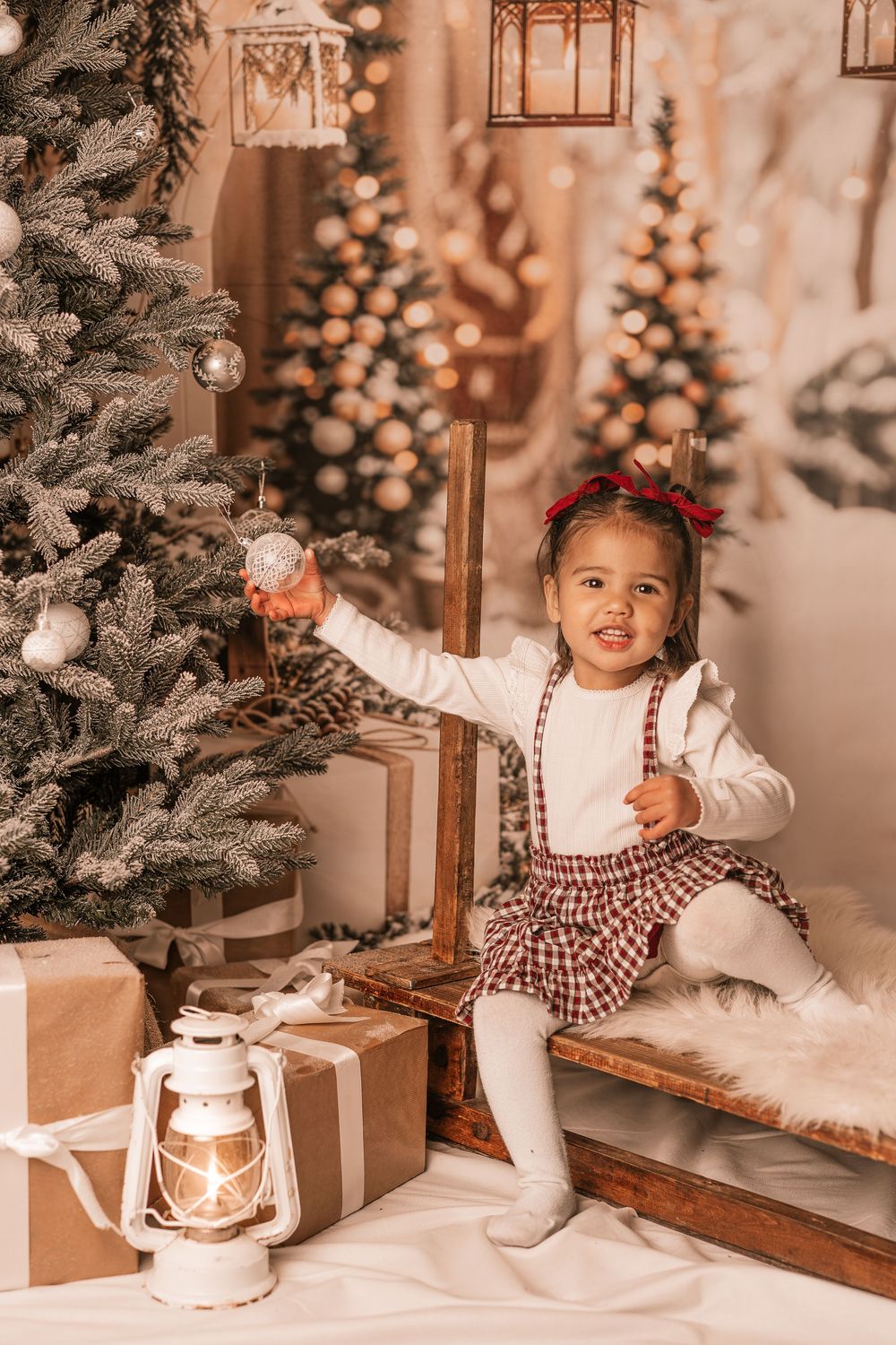 Child plays with vintage lantern decorations by Christmas tree surrounded by wrapped gifts in sepia tones.