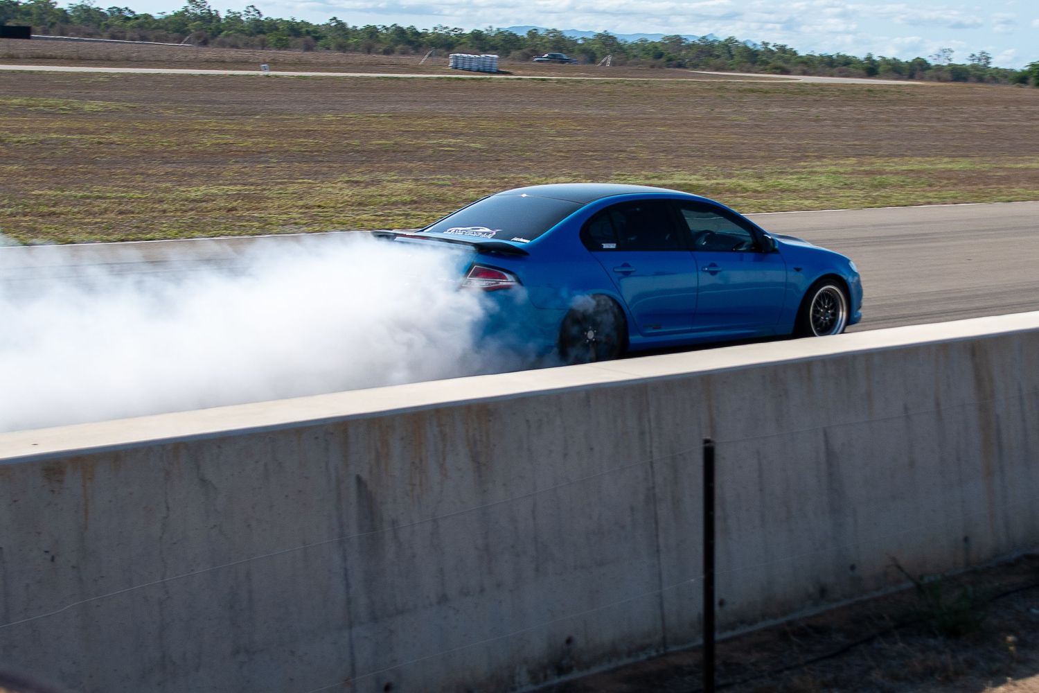 A blue Subaru WRX performs a drift maneuver on a race track, creating a cloud of tire smoke.