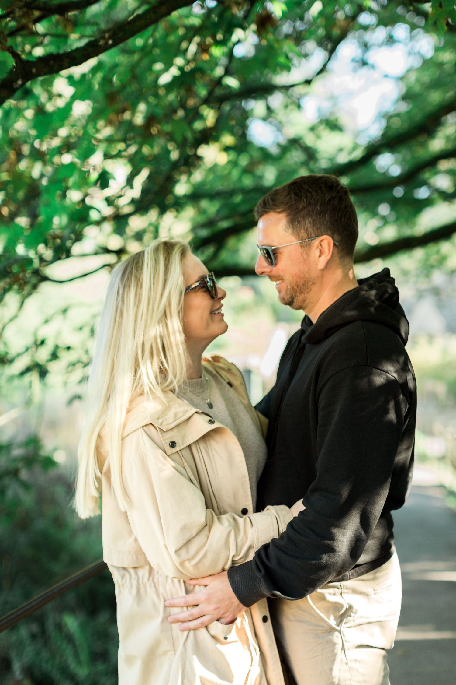 An engaged couple autumnal clothing share an intimate moment under green trees in Bibury Cotswolds. Hayley Elizabeth Photography