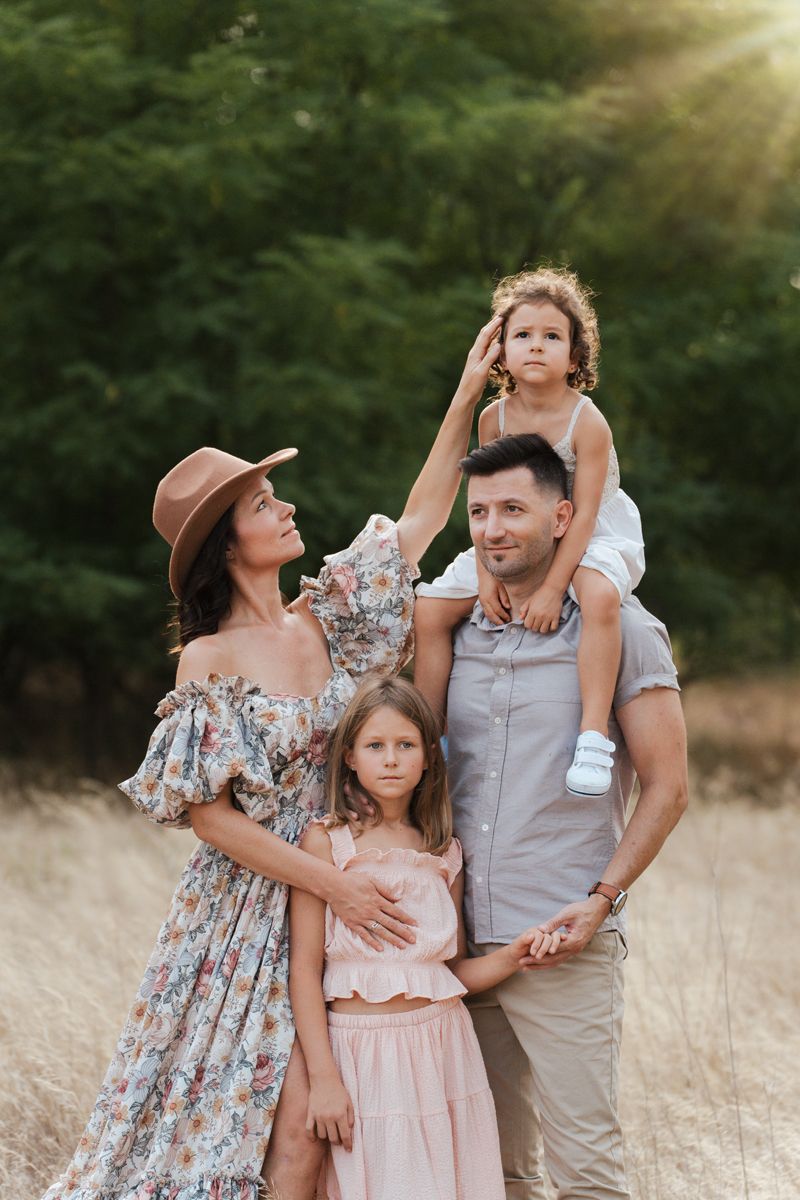 A loving family poses together in a golden field at sunset wearing coordinated pastel and floral outfits in Rouse Hill Regional Park