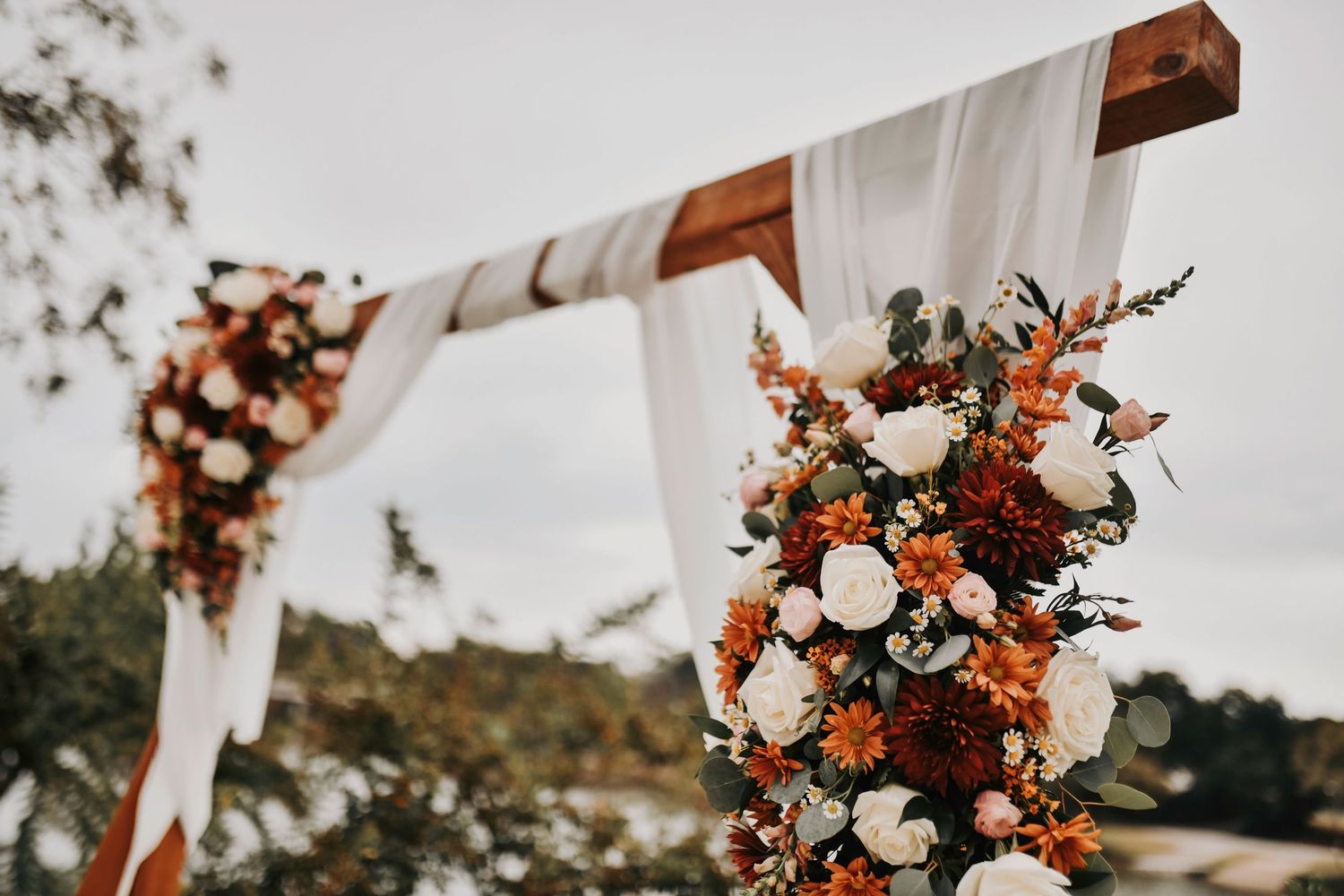 the wedding altar is adorned with an ivory linen drapery and covered in fall florals and wildflowers