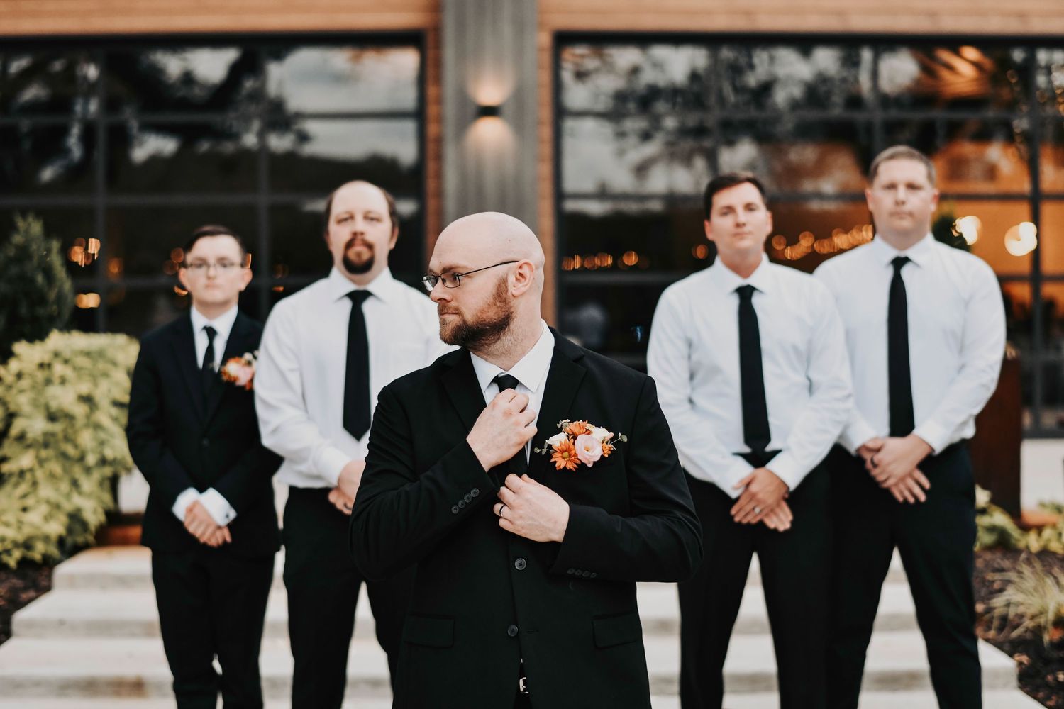 dapper groomsmen pose with the groom in a black tie and suit in front of the rivers edge at tip top