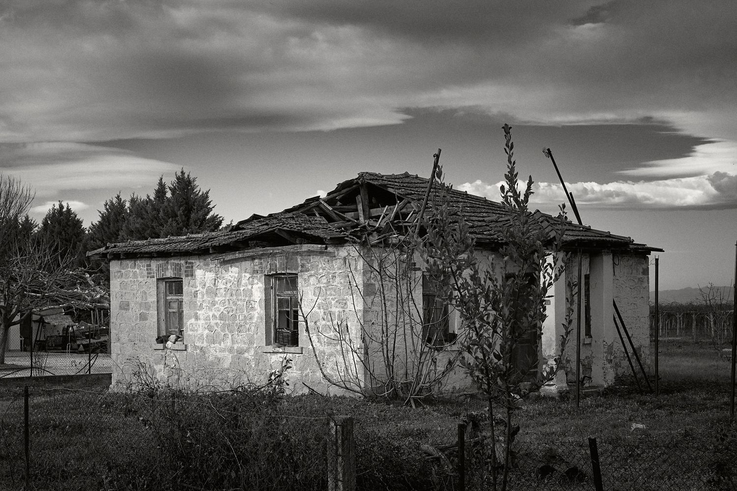 A series of abandoned rural buildings and structures photographed in black and white under dramatic cloudy skies.