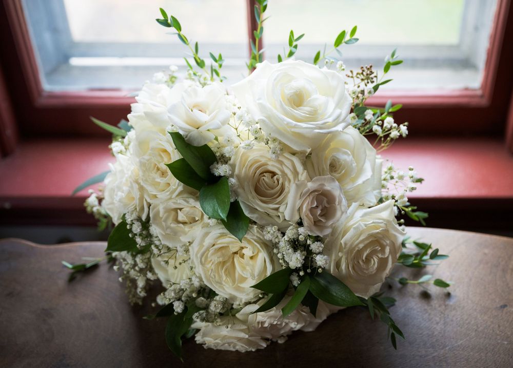 Elegant white rose wedding bouquet with delicate greenery sits by a window.